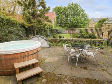 A patio area with a wooden hot tub metal table and chairs surrounded by greenery at White Swan Cottage in Alnwick