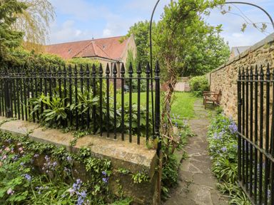 A garden with a stone pathway flowers and benches at White Swan Cottage in Alnwick