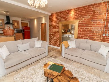 A living room with two beige sofas and a wooden coffee table on a rug with an exposed brick wall and a large mirror at The Fullerton in Belsay