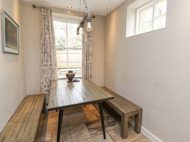 A dining area with a wooden table and benches near windows with patterned curtains at The Fullerton in Belsay
