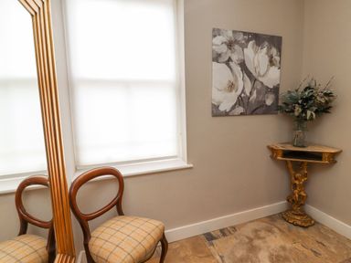 A corner of a room with a wooden chair and large mirror beside a window a ornate gold corner table with a vase of flowers and a floral painting on the wall at The Fullerton in Belsay