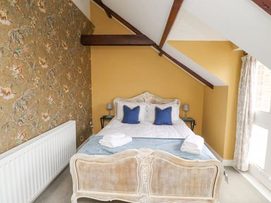 A bedroom with a bed with blue pillows and folded towels yellow walls a window and floral wallpaper at The Fullerton in Belsay