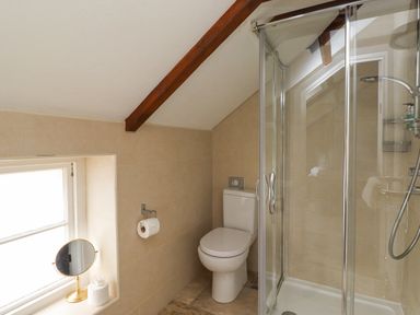 A bathroom with a toilet, a glass shower enclosure, a window with a round mirror and a tissue box on the windowsill at The Fullerton in Belsay