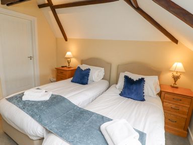 A bedroom with two single beds with blue pillows and bed runners with wooden bedside tables and lamps at The Fullerton in Belsay