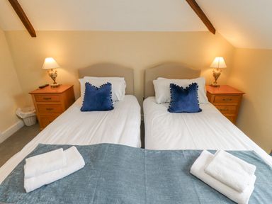 Two single beds with blue pillows white towels on a blue runner and wooden bedside tables with lamps in a bedroom at The Fullerton in Belsay