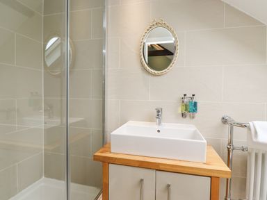 A bathroom with a shower enclosure a rectangular sink on a wooden countertop a round mirror and wall-mounted soap dispensers at The Fullerton in Belsay