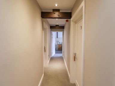 A hallway with beige walls and carpeted floor with doors on both sides and a wooden beam overhead at The Fullerton in Belsay