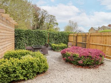 An outdoor garden area with patio furniture a wooden fence and green and pink shrubs at The Fullerton in Belsay