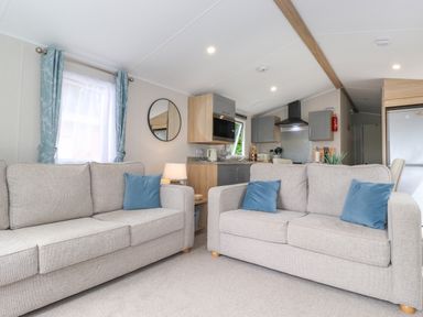 A living room with two beige sofas and blue cushions facing a kitchen area at Eltons Escape Pony Meadow 3 White Cross Bay near Windermere