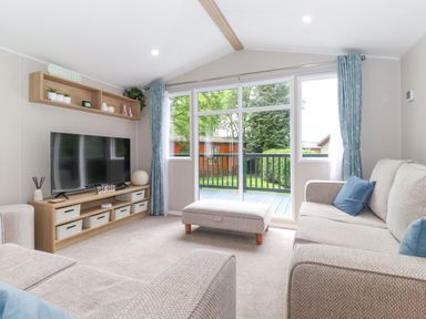 A living room with a television a beige couch blue pillows and sliding glass doors at Eltons Escape in Pony Meadow 3 White Cross Bay near Windermere