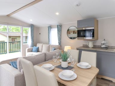 A dining table with plates and glasses next to a sofa and kitchen area at Elton's Escape Pony Meadow 3 White Cross Bay near Windermere