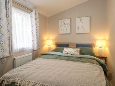 A bedroom with a bed bedside tables lamps and abstract wall art at Elton's Escape in Pony Meadow 3 White Cross Bay near Windermere