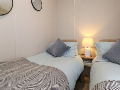 A bedroom with two single beds side by side a nightstand with a lamp between them and two round mirrors on the wall at Eltons Escape in Pony Meadow 3 White Cross Bay near Windermere