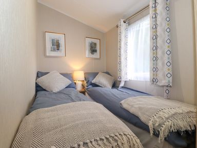 A bedroom with two single beds a lamp on a nightstand and patterned curtains at Eltons Escape Pony Meadow 3 White Cross Bay near Windermere