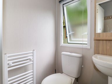 A bathroom with a toilet sink mirror towel radiator and an open window at Eltons Escape in Pony Meadow 3 White Cross Bay near Windermere