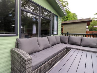 An outdoor seating area with a grey cushioned corner sofa and a matching grey table at Eltons Escape in Pony Meadow 3 White Cross Bay near Windermere