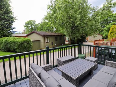 An outdoor patio with gray cushioned wicker furniture and a table overlooking cabins and trees at Eltons Escape Pony Meadow 3 White Cross Bay near Windermere