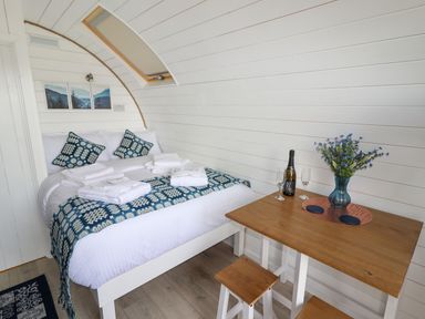 A bedroom with a bed covered in white linens and blue patterned cushions next to a wooden table with a vase of flowers and a bottle of drink at Moel Famau in Bryniau Clwyd near Denbigh