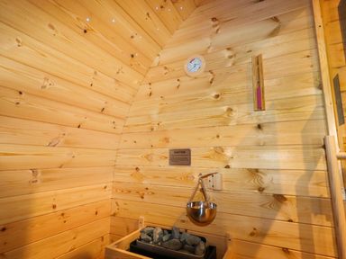 An interior of a wooden sauna with heater stones, a metal water bowl, a thermometer, and a hygrometer at Moel Famau in Bryniau Clwyd near Denbigh