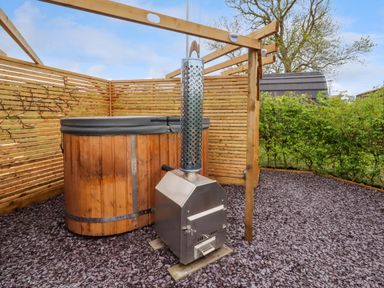 An outdoor hot tub with a wood burning stove on a gravel surface surrounded by wooden fencing and greenery at Moel Famau in Bryniau Clwyd near Denbigh