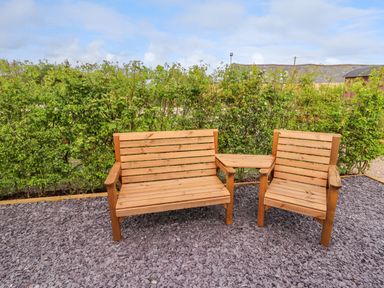 An outdoor seating area with a wooden bench and chair connected by a small table with greenery in the background at Moel Famau in Bryniau Clwyd near Denbigh