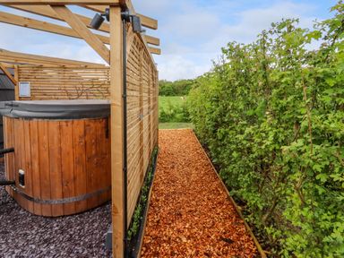 An outdoor wooden hot tub next to a wooden privacy screen with a wood chip pathway and green bushes at Moel Famau Bryniau Clwyd near Denbigh
