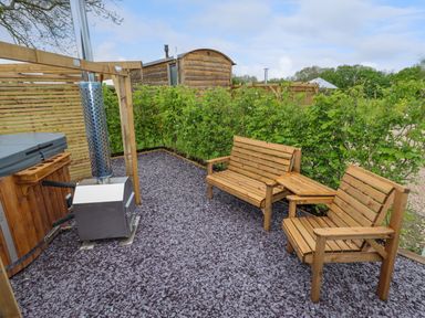 An outdoor seating area with wooden benches and a hot tub with a chimney at Moel Arthur in Bryniau Clwyd near Denbigh