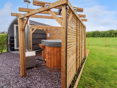 An outdoor wooden hot tub with privacy panels on a bed of slate chippings next to a small building in a grassy field at Moel Arthur in Bryniau Clwyd near Denbigh