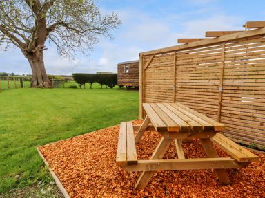 A wooden picnic table on wood chips next to a wooden fence in a grassy backyard at Moel Arthur in Bryniau Clwyd near Denbigh