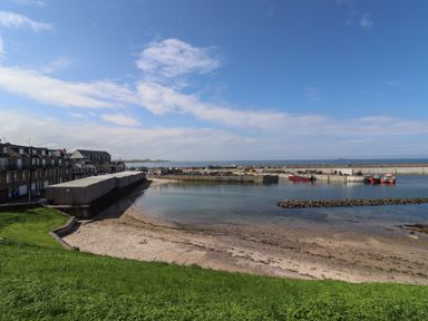A harbor with boats docked near a sandy shore and buildings along the waterfront at Greenlee House in Seahouses