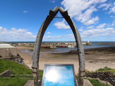A beach with a harbor and boats framed by a large whale jaw bone arch at Greenlee House in Seahouses