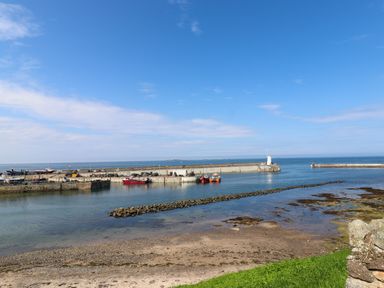 A view of a small harbor with boats docked and a breakwater extending into the sea at Greenlee House in Seahouses
