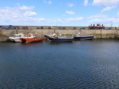 A harbor with six boats docked and cars parked along a concrete wall in the background at Greenlee House in Seahouses