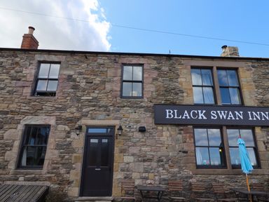 The stone exterior of a building with multiple windows a door and outdoor tables and chairs at Black Swan Inn
