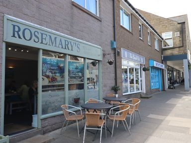 A cafe with outdoor tables and chairs next to shops on a sidewalk