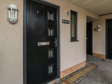 A black front door with small windows and mail slot on a beige wall with a light fixture and a window at Greenlee House in Seahouses