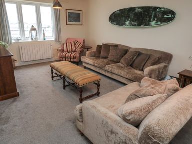 A living room with two sofas a striped armchair a long bench a surfboard mounted on the wall and a window with curtains at Greenlee House in Seahouses