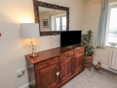 A wooden cabinet with a lamp and television in a room with a window and curtains at Greenlee House in Seahouses