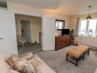 A living room with a beige sofa, wooden cabinet with a TV, a window, an upholstered bench, and a doorway leading to another room at Greenlee House in Seahouses