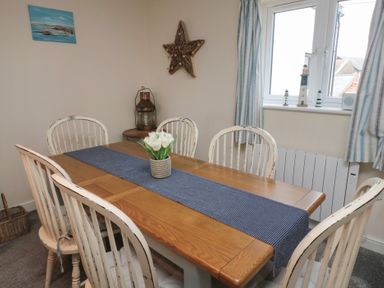 A dining area with a wooden table and six white chairs with a blue table runner and a vase of white flowers at Greenlee House in Seahouses