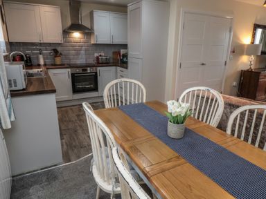 A kitchen with white cabinets and wooden countertops next to a wooden dining table with white chairs and a flower vase at Greenlee House in Seahouses