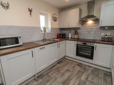 A kitchen with white cabinets wooden countertop microwave oven stove and toaster at Greenlee House in Seahouses