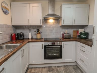 A kitchen with white cabinets a wooden countertop a stainless steel oven a sink and kitchen appliances at Greenlee House in Seahouses