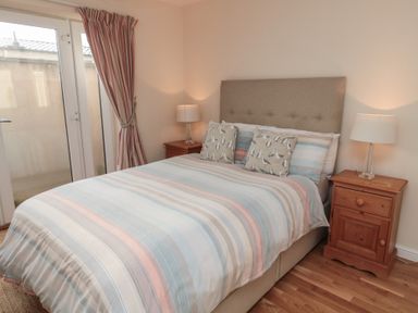 A bedroom with a bed with striped bedding and bird print pillows with two wooden nightstands and lamps at Greenlee House in Seahouses