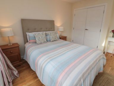 A bedroom with a double bed striped bedding two bedside tables with lamps and a double door wardrobe at Greenlee House in Seahouses