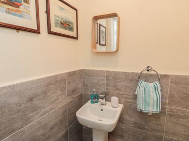 A small bathroom corner with a pedestal sink a mirror hand towel and framed boat pictures on the wall at Greenlee House in Seahouses