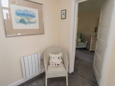 A corner with a wicker chair and cushions near a heater and two pictures on the wall at Greenlee House in Seahouses