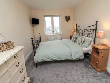 A bedroom with a metal bed frame two wooden bedside tables lamps a window and a dresser at Greenlee House in Seahouses