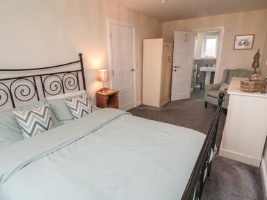 A bedroom with a bed a nightstand with a lamp a wardrobe a chair and an open door leading to a bathroom at Greenlee House in Seahouses