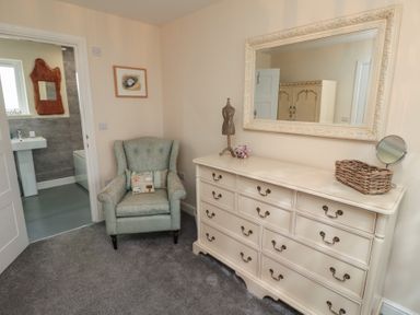 A room with a green armchair a cream dresser with a large mirror and a doorway leading to a bathroom at Greenlee House in Seahouses